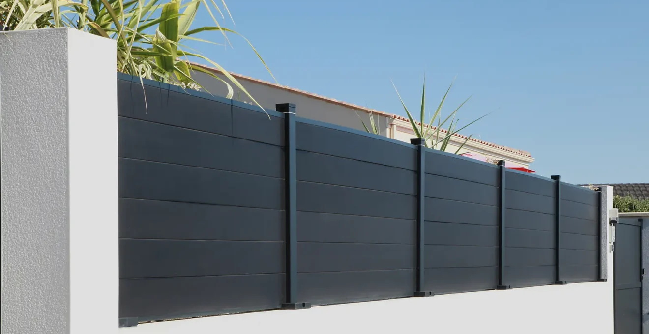 Des mains gantées rincent une lame d'aluminium au tuyau d'arrosage.